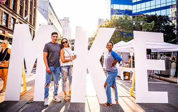 Smiling people holding MKE letters.